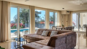A spacious living room with a large sofa, a dining area, and a view of a swimming pool.
