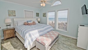 A bedroom with a bed, bedside tables, a ceiling fan, a bench, and a view of the ocean. - Dune Alright, Oceanfront House in Emerald Isle, NC! (Emerald Isle)