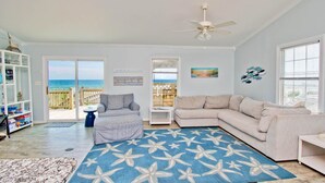 A living room with a view of the beach, a ceiling fan, and a large rug. - Dune Alright, Oceanfront House in Emerald Isle, NC! (Emerald Isle)