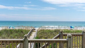 A wooden boardwalk leading to a beach with umbrellas and the ocean in the background. - Dune Alright, Oceanfront House in Emerald Isle, NC! (Emerald Isle)