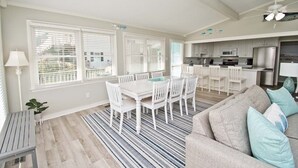 A modern kitchen with white cabinets, stainless steel appliances, and a dining area with a white table and chairs. - Dune It Whale, Oceanfront House In Emerald Isle, NC! (Emerald Isle)