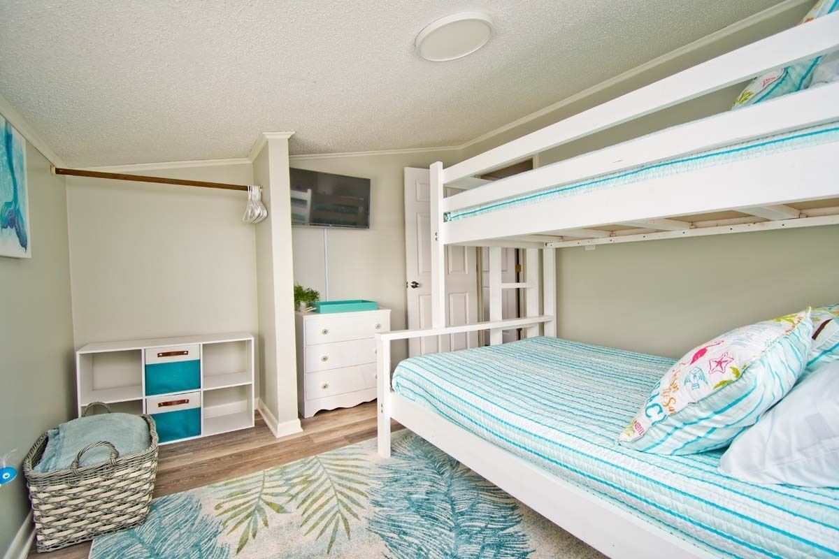 A bunk bed room with a white and blue striped bedspread, a white dresser, a small white shelf, and a woven basket.