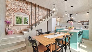 Eine moderne Küche mit einer zentralen Kochinsel, einem Essbereich mit Holztisch und -stühlen sowie einer Treppe mit freiliegenden Backsteinwänden.