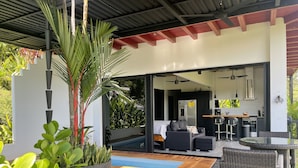 Un espacio exterior moderno con piscina, asientos y una cocina visible a través de un ventanal abierto.