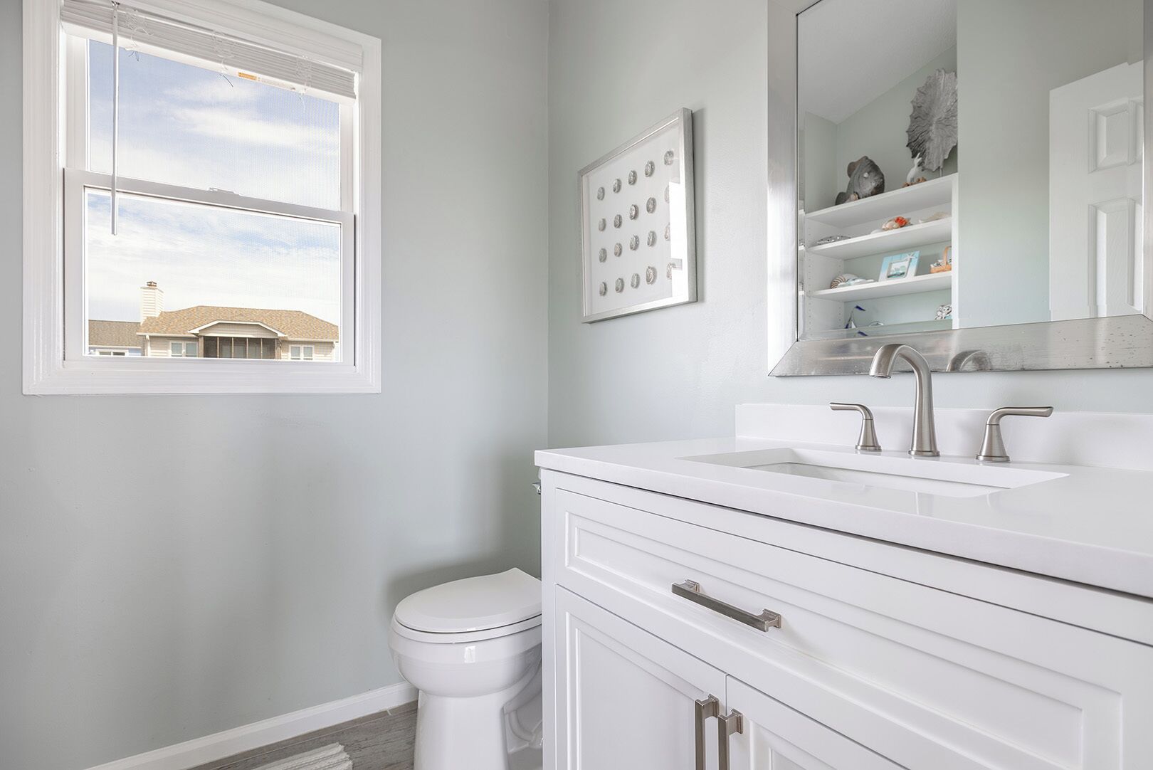 A bathroom with a white vanity, a large mirror, and a window.