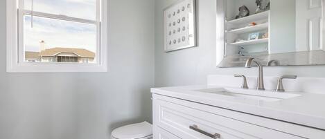 A bathroom with a white vanity, a large mirror, and a window.