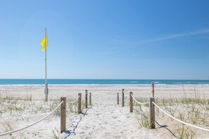 Ein Pfad aus Sandstrand mit einer gelben Fahne, der zum Meer führt.
