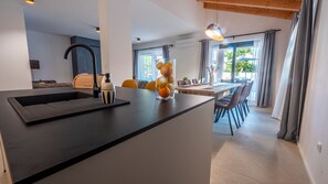 A modern kitchen with a central island, a dining area with a table and chairs, and a view of the outdoors through large windows. - Villa Alves by Villas Guide (Tar)