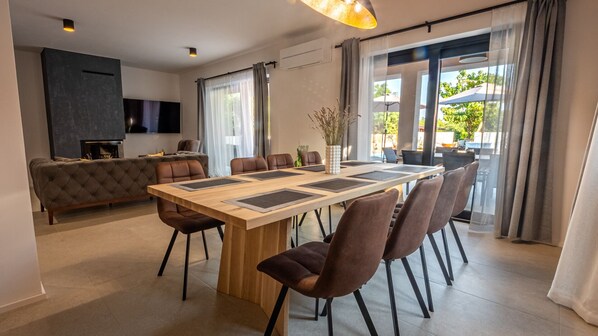 A modern dining area with a wooden table, brown chairs, and a sofa in the background.