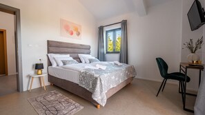 A bedroom with a bed, bedside table, lamp, chair, window, and artwork.