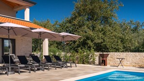 A poolside area with lounge chairs and umbrellas, a stone wall, and a clear blue sky.