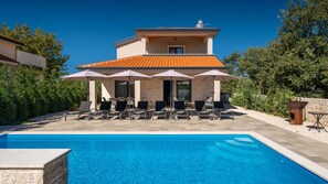 A poolside area with lounge chairs and umbrellas, a clear blue pool, and a building with a tiled roof. - Villa Alves by Villas Guide (Tar)