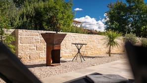 An outdoor barbecue grill, a stone wall, and a small table with a chair.