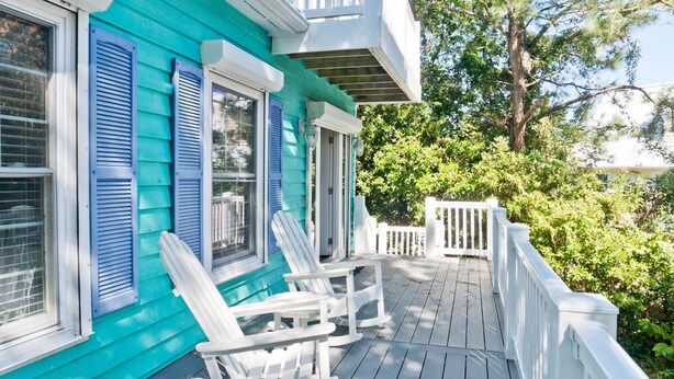 A turquoise house with white shutters, a porch with white railings, and two white Adirondack chairs.