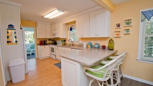 A kitchen with white cabinets, a granite countertop, and a small island with bar stools.
