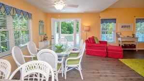 A dining area with a glass table and white wicker chairs, a red sofa, and a ceiling fan.