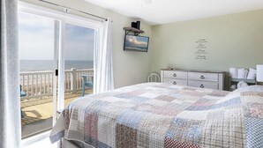 Une chambre avec un grand lit, un ventilateur de plafond, une commode et une vue sur l’océan.