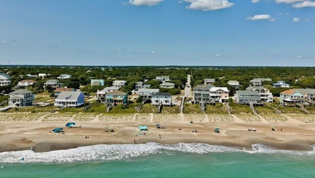 Un quartier résidentiel situé sur la côte, avec des maisons construites le long de la plage, une plage de sable et une vue dégagée sur l’océan.