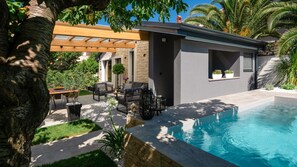 Ein moderner Poolbereich im Freien mit einer Pergola, Sitzgelegenheiten und einer Steinmauer.