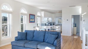 A modern living room with a blue sofa, a dining area with a table and chairs, and a kitchen in the background. - Flip Flop Inn, Almost Oceanfront Duplex in Emerald Isle, NC! (Emerald Isle)
