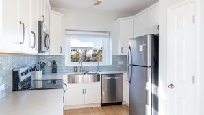 A modern kitchen with white cabinets, stainless steel appliances, a window with a view, and a ceiling fan. - Flip Flop Inn, Almost Oceanfront Duplex in Emerald Isle, NC! (Emerald Isle)