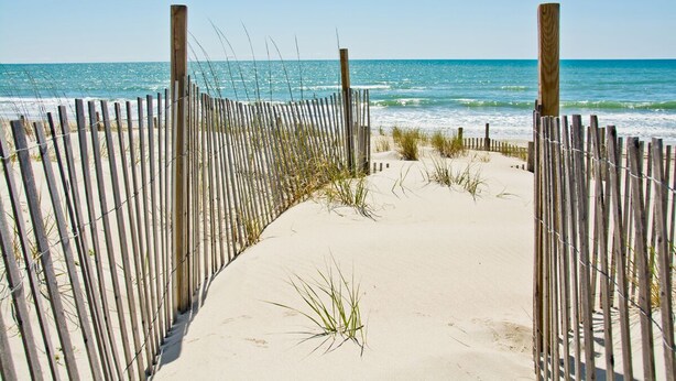 A sandy beach path with a wooden fence and grass in the foreground, leading to the ocean. - Footprints East, Oceanfront Duplex in Emerald Isle, NC! (Emerald Isle)