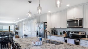 A modern kitchen with white cabinets, a granite countertop, stainless steel appliances, and pendant lighting. - Footprints East, Oceanfront Duplex in Emerald Isle, NC! (Emerald Isle)