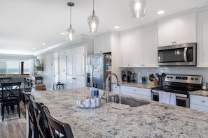 A modern kitchen with white cabinets, a granite countertop, stainless steel appliances, and pendant lighting. - Footprints East, Oceanfront Duplex in Emerald Isle, NC! (Emerald Isle)