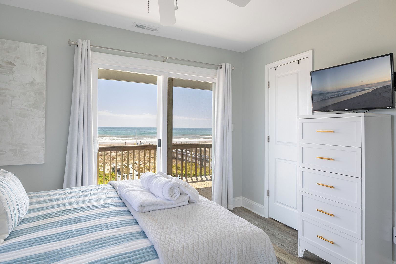 Un dormitorio con cama, televisor, cómoda y balcón con vista a la playa.