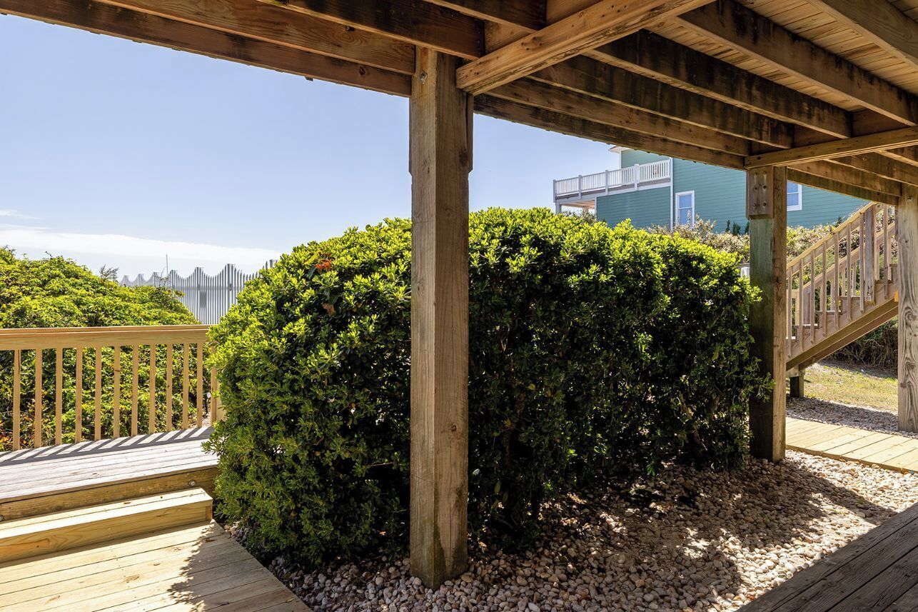 A wooden deck with a wooden railing, a wooden pergola, and a well-maintained hedge.