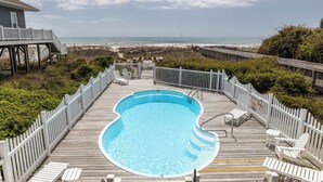 Une piscine entourée d’une terrasse en bois, de chaises blanches et offrant une vue sur la plage.