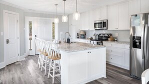 Une cuisine moderne avec des meubles blancs, un îlot central doté de tabourets, des appareils en acier inoxydable et un éclairage suspendu.