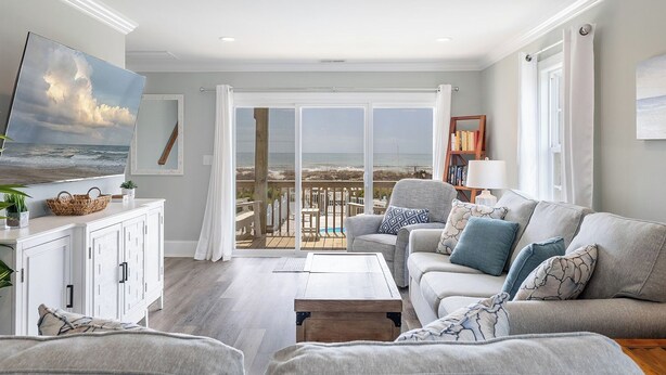Un salon avec vue sur la plage, un canapé blanc, une table basse et une bibliothèque.