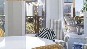 Um quarto claro com uma mesa branca, cadeiras quadriculas amarelas e brancas, um sofá listrado e uma luminária pendente trançada.