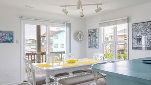 Un espace de repas lumineux, avec une table et des chaises blanches, un comptoir bleu et de grandes fenêtres donnant sur le quartier.