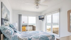 Une chambre avec un lit, un ventilateur de plafond, une télévision et une vue sur la plage.