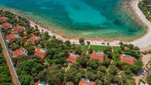An aerial view of a coastal residential area with houses, a beach, and clear blue waters.
