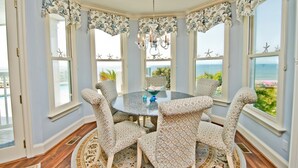 A dining area with a round table, patterned chairs, and a view of the ocean. - Gone With The Waves, Oceanfront House in Emerald Isle, NC! (Emerald Isle)