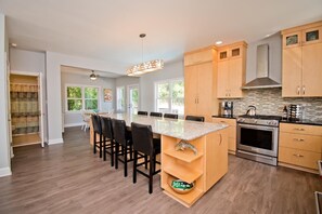 Una cocina moderna con armarios de madera, una isla central con taburetes de bar, horno empotrado y un amplio ventanal que proporciona luz natural.