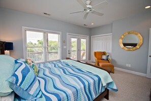 A bedroom with a bed, a chair, a ceiling fan, and a large window. - Grace Appearing, Oceanside House in Emerald Isle, NC! (Emerald Isle)