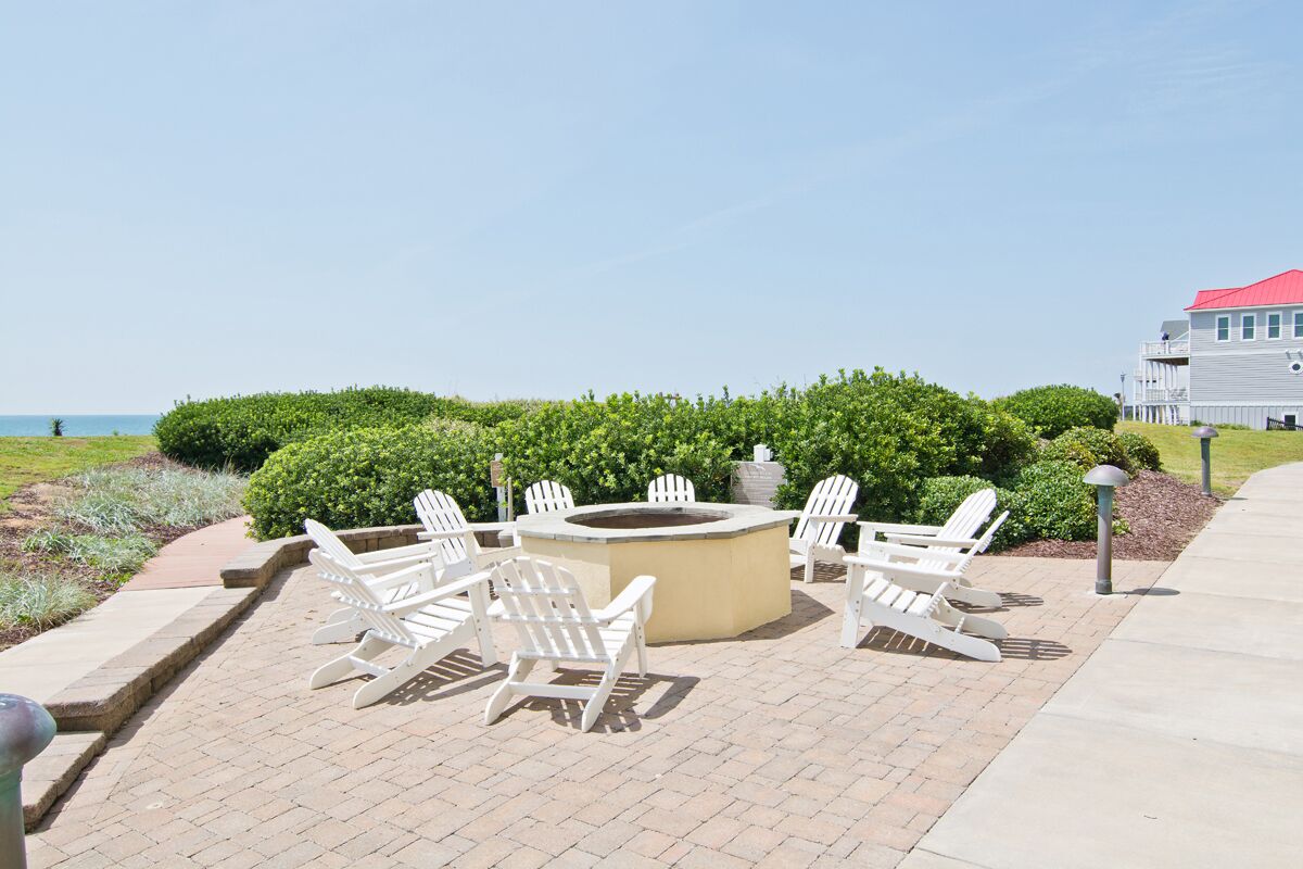 Un patio con sillas Adirondack y una fogata, rodeado de vegetación y vistas al océano.
