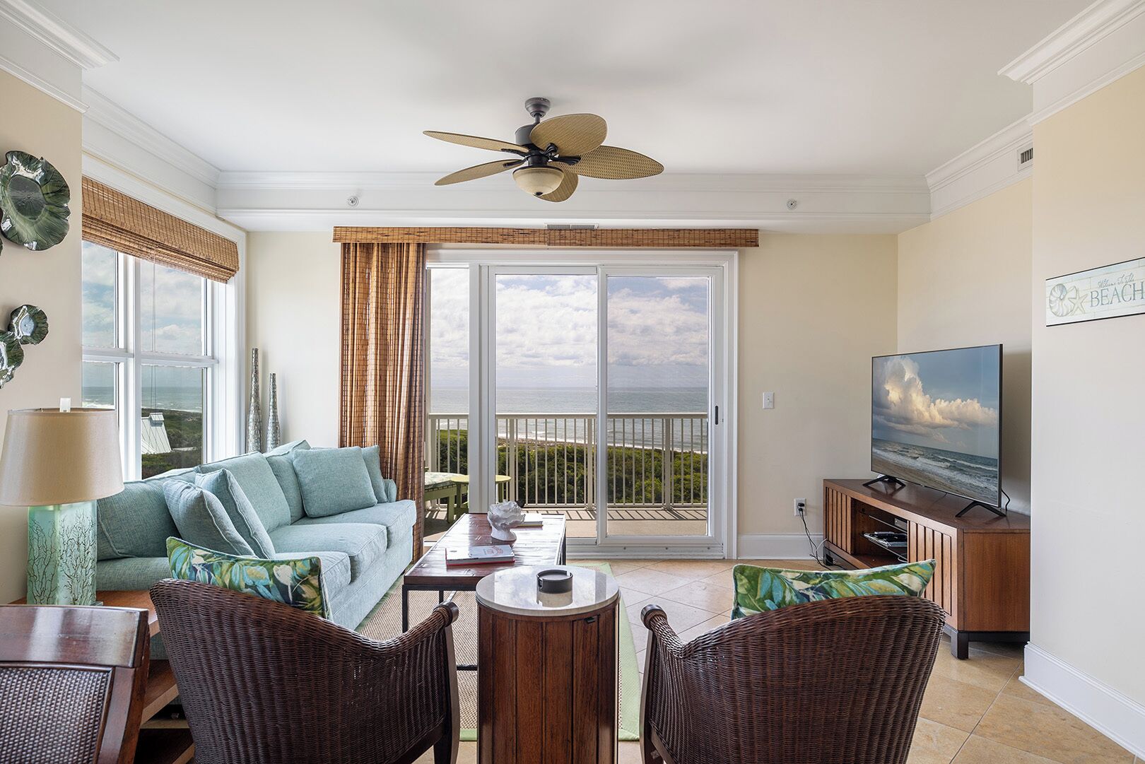 A living room with a sofa, chairs, a TV, and a balcony with a view of the ocean.