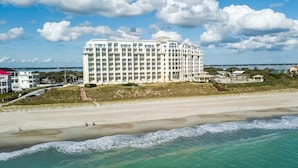 A large, multi-story hotel with a white facade, located near a beach with visible waves. - Grande Villas D-3, Oceanfront Condo in Indian Beach, NC! (Indian Beach)