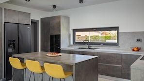 Une cuisine moderne dotée d’un îlot central, d’un four encastré et d’une fenêtre donnant sur un jardin.