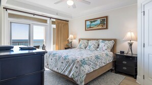 Een slaapkamer met een bed, nachtkastjes, een bureau, een plafondventilator en uitzicht op de oceaan.