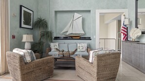 Een woonkamer met rieten meubilair, een decoratie van een zeilboot en een vlag.