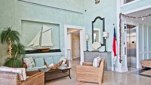A spacious lobby with wicker furniture, a sailboat decoration, a flag, and a modern elevator. - Grande Villas M-3, Oceanfront Condo in Indian Beach, NC! (Indian Beach)