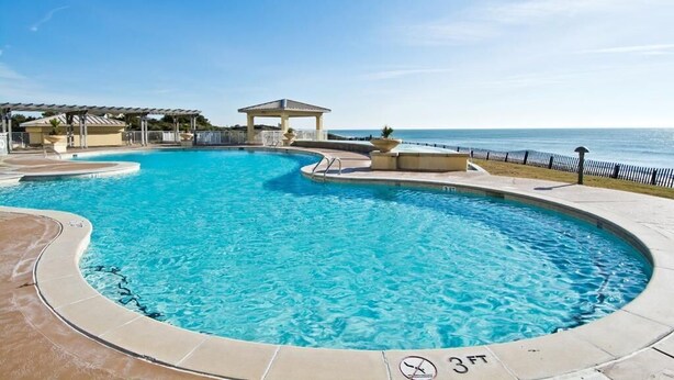 A swimming pool with a 3ft depth marker, surrounded by a deck area with a gazebo and a view of the sea. - Grande Villas M-3, Oceanfront Condo in Indian Beach, NC! (Indian Beach)