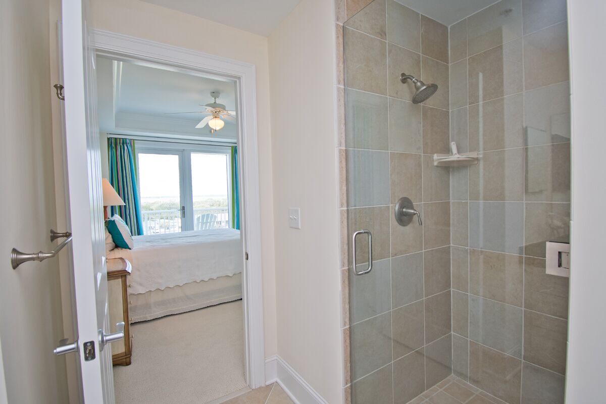 A bathroom with a glass shower enclosure, a window with curtains, and a door with a towel rack.