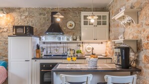 A kitchen with stone walls, white cabinetry, a black range hood, and pendant lights. - Villa Nonni by Villas Guide (Cerion)